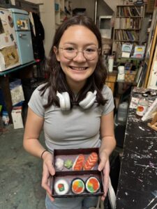 Smiling girl holding a sushi meal box indoors.