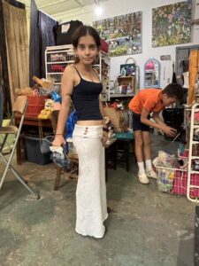 Young woman in white pants and black top posing indoors.