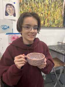 Young person holding a large bowl with a smile in an art studio.