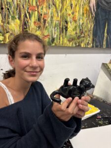 A young woman holding a small black sculpture in an art studio.