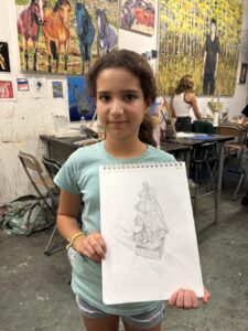 Young girl proudly displays her detailed pencil drawing in an art studio.