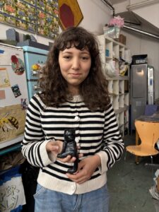 A young woman with curly hair holding a small object in a workshop.