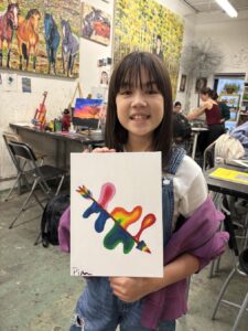 Young woman proudly holding a colorful painted canvas with abstract shapes.