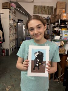 A young girl proudly holds a photo of a black dog indoors.