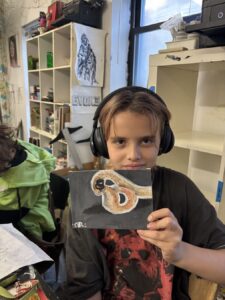 Child holding a drawing of a snake, wearing headphones.