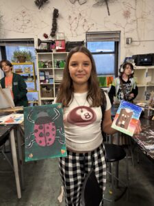 A girl proudly holds up her colorful paintings in an art studio.
