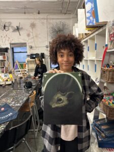 Young artist proudly displays a backpack with a rabbit design in a creative studio.