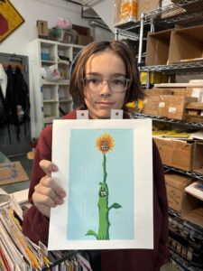 Young person proudly holding artwork of a cactus with a flower.