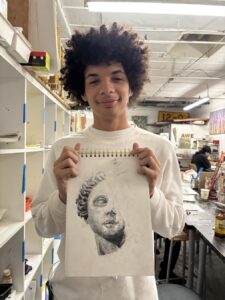 Young man holding a detailed portrait drawing in an art studio.
