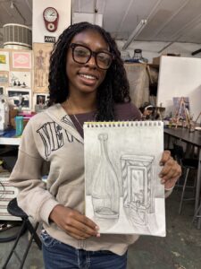 Woman proudly displays her detailed pencil sketch in an art studio.