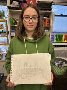 Young girl in glasses holding a notebook with drawings.