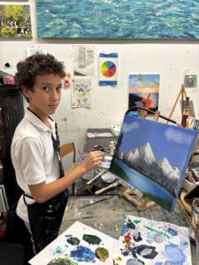 Young artist painting a mountain landscape in a classroom.