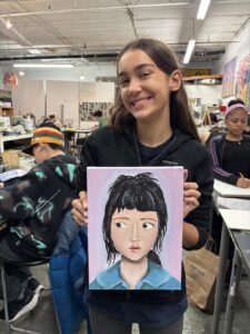 A young girl proudly holds a painting of a girl with short hair.