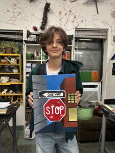 Young person holding a colorful handmade sign with a stop symbol.