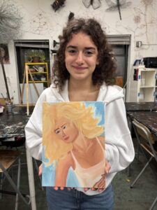 Young woman holding a painting of a blonde woman.