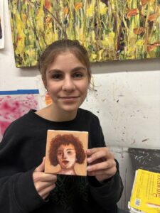 A young woman holding a portrait of a person with curly hair.