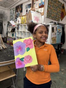 Girl proudly holds colorful flower painting in an art studio.