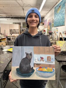 Person smiling and holding a painting of a cat and breakfast items.