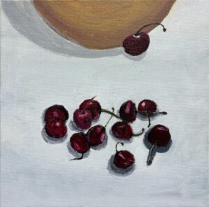 A small group of cherries on a light surface near an object.