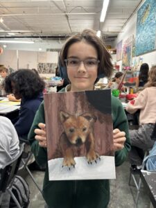 Student proudly shows realistic dog painting in art class.