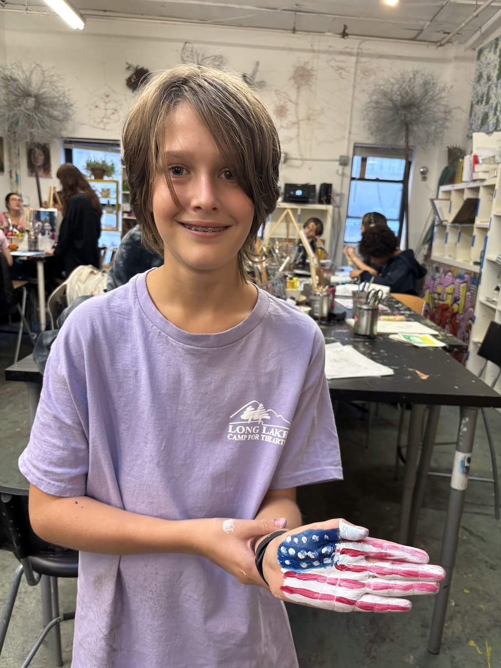 A smiling child holding a patriotic American flag-themed craft indoors.