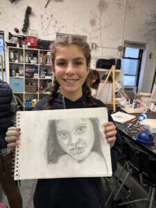 Young artist proudly displays a detailed pencil portrait in an art studio.